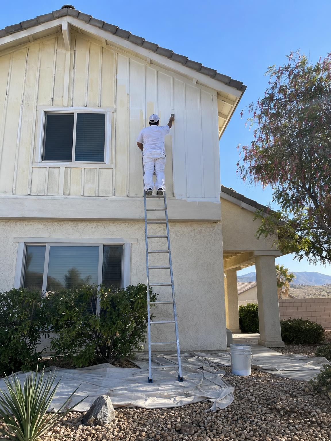 Painter up on the second story of a white board-and-batten house